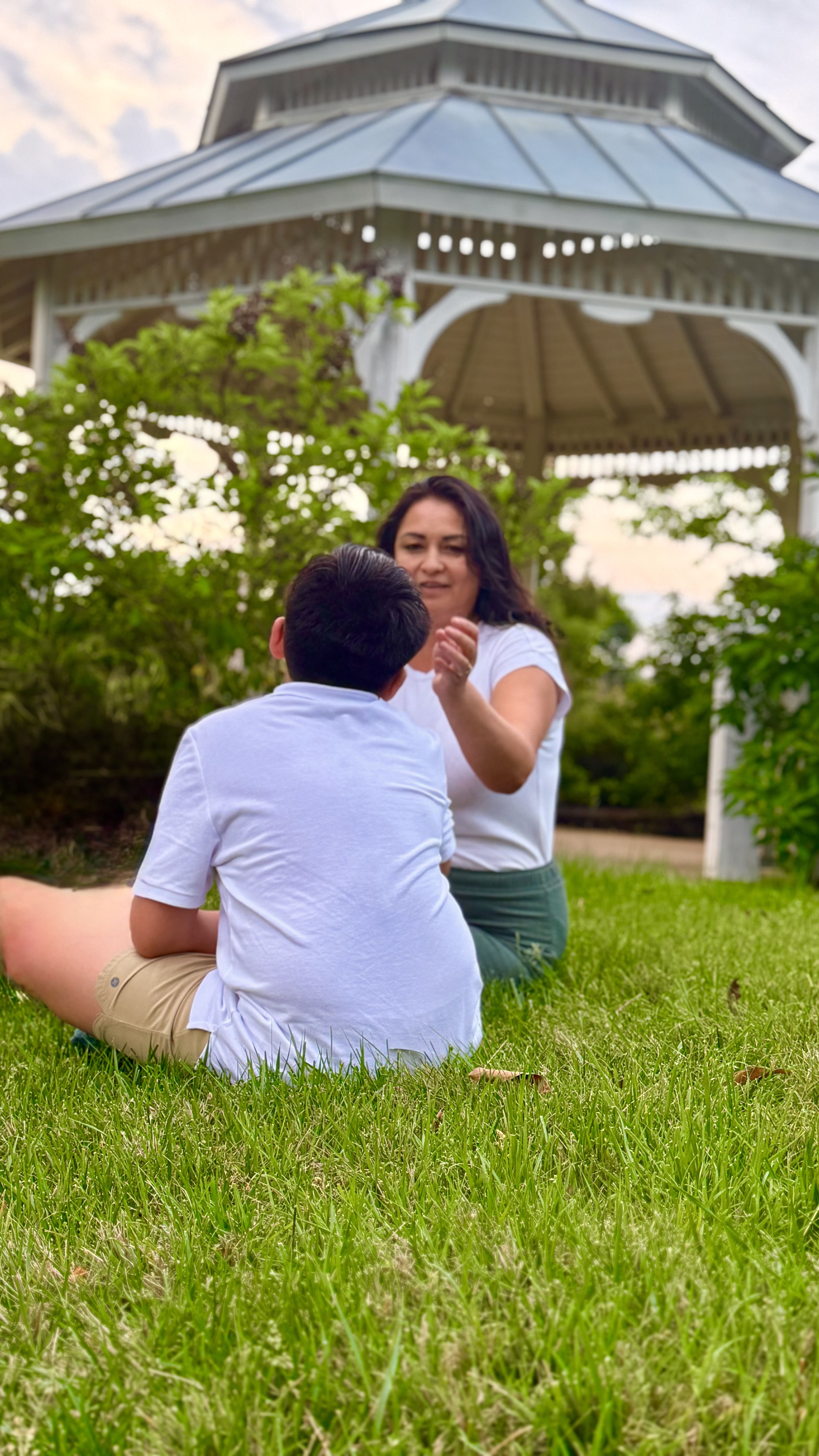 Diana sitting in the grass talking with her son by a gazebo