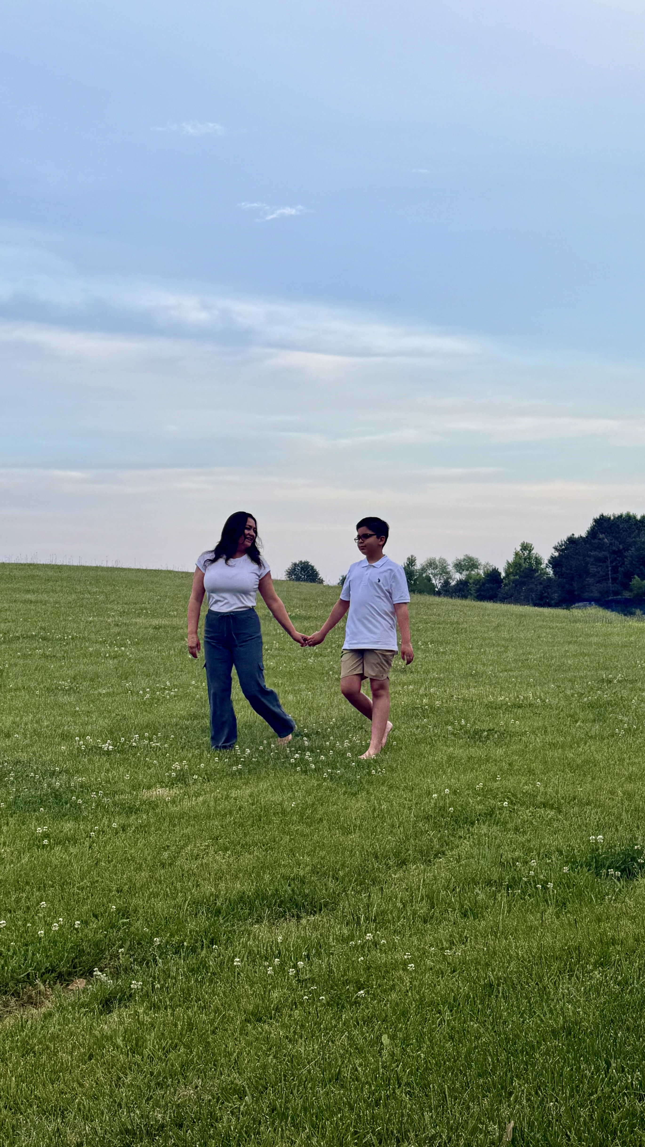 Diana walking hand in hand with her son across an open field at golden hour